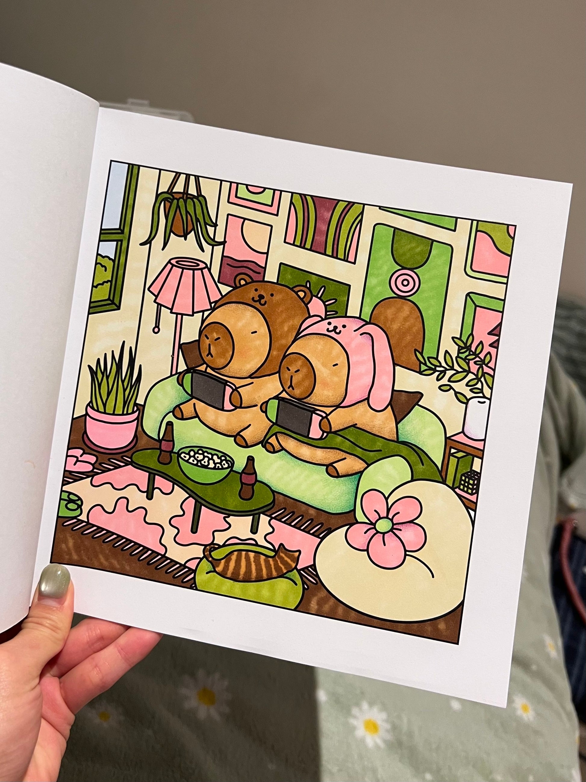 A sample illustration of two capybaras in a cozy room with a lamp and plants, made with alcohol markers.